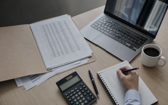 Bureau d'un candidat au DEC : ordinateur portable, dossier de feuilles de calcul annotées et calculatrice